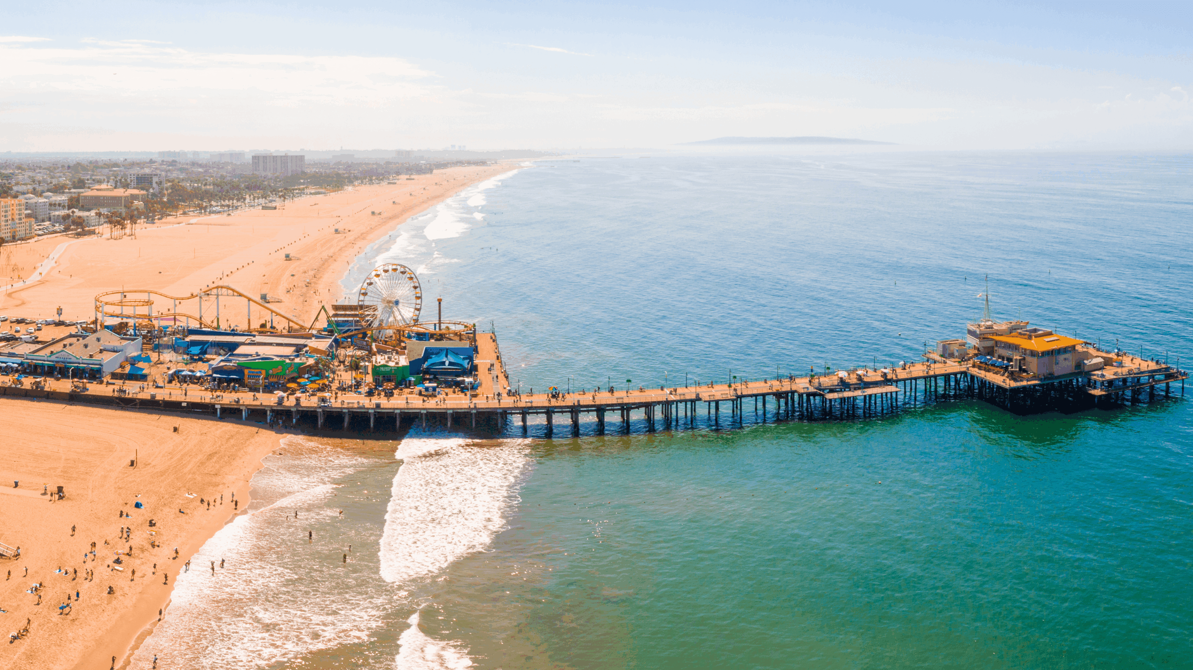 Aerial view of a long pier extending into the ocean from a sandy beach.