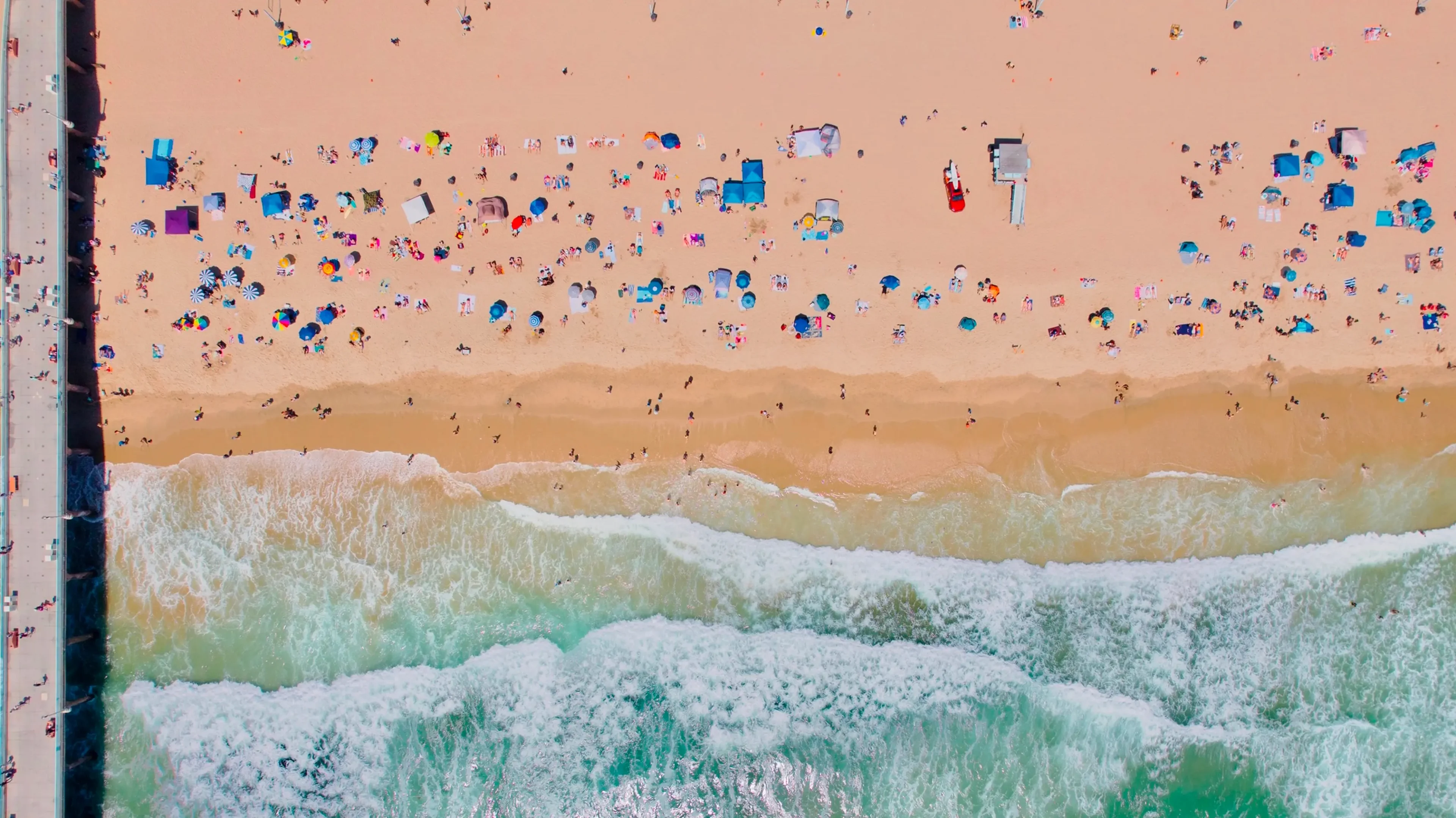 Aerial view of crowded beach with colorful umbrellas and waves.